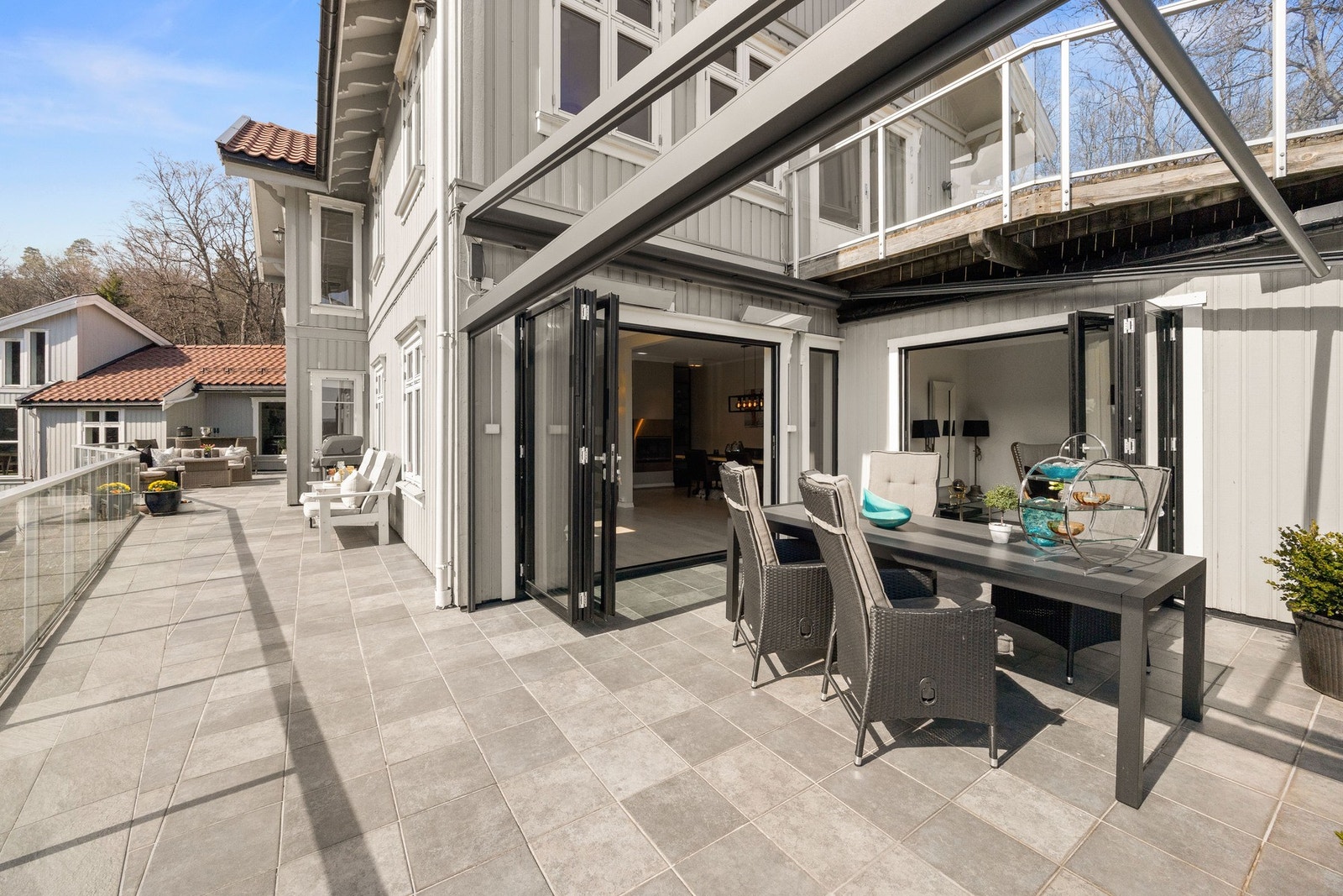 Romslig terrasse med flislagt gulv, glassrekkverk og direkte utgang fra stue. Elektrisk pergola med tak og vegger Galleribilde