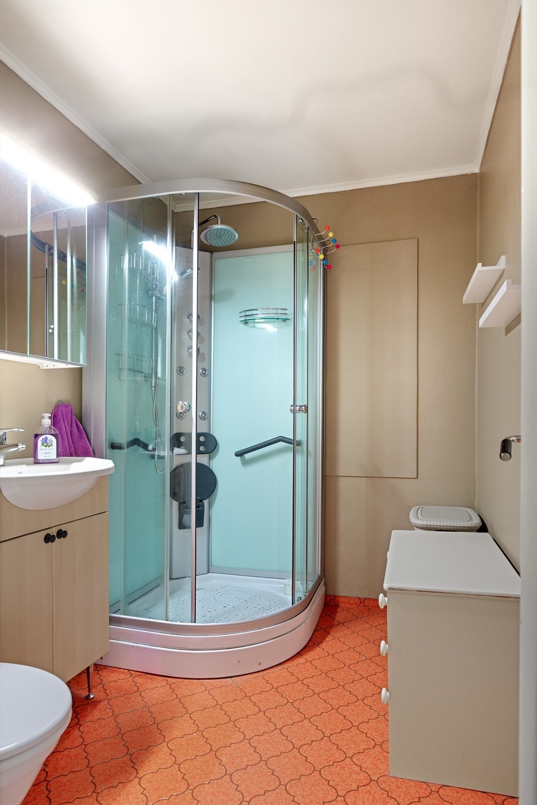 Badet i 1. etasje har vinylbelegg på gulv, våtromstapet på vegger og nyere innredning med servantskap og vegghengt speilskap med lys. Dusjkabinett og nyere gulvstående toalett. Galleribilde