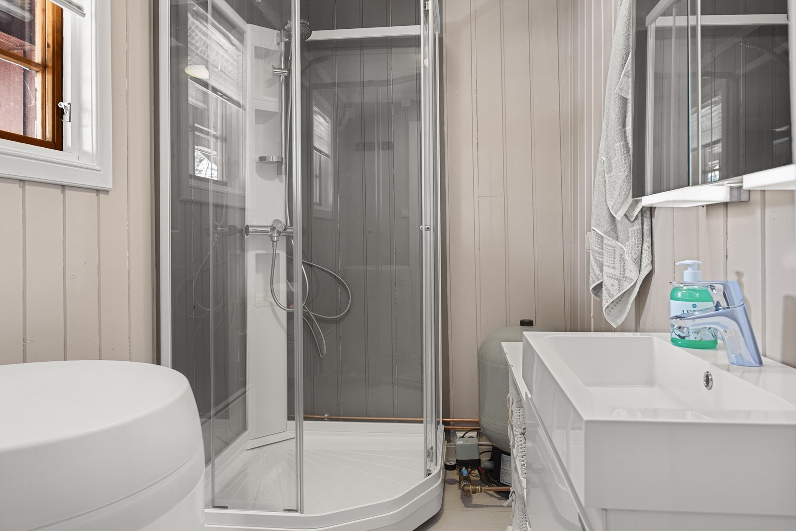 Det lysmalte badet har tregulv og panelte vegger og er fra byggeår. På badet er det innredning med heldekkende servant og overskap med speildører, samt et frittstående dusjkabinett. Trykktank og en varmtvannstank på ca. 120 liter. Galleribilde
