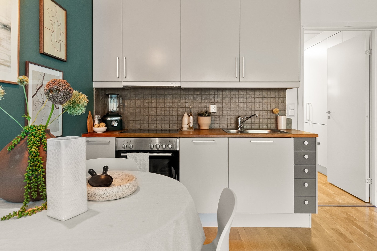 Innredning bestående av hvite glatte fronter, benkeplate i heltre og nedfelt kum i rustfritt stål. Backsplash av mosaikkfliser og lys under overskap. Galleribilde