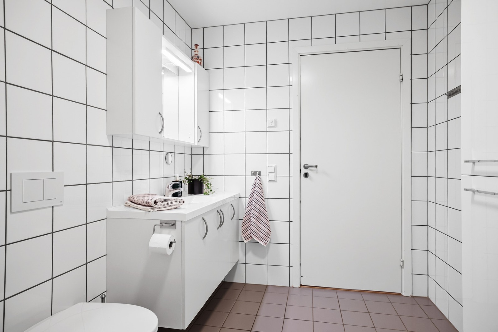 Badet er innredet med en moderne baderomsinnredning med servant, et vegghengt skap for ekstra oppbevaring, gulvstående toalett og et praktisk dusjhjørne med innfellbare dører. Galleribilde