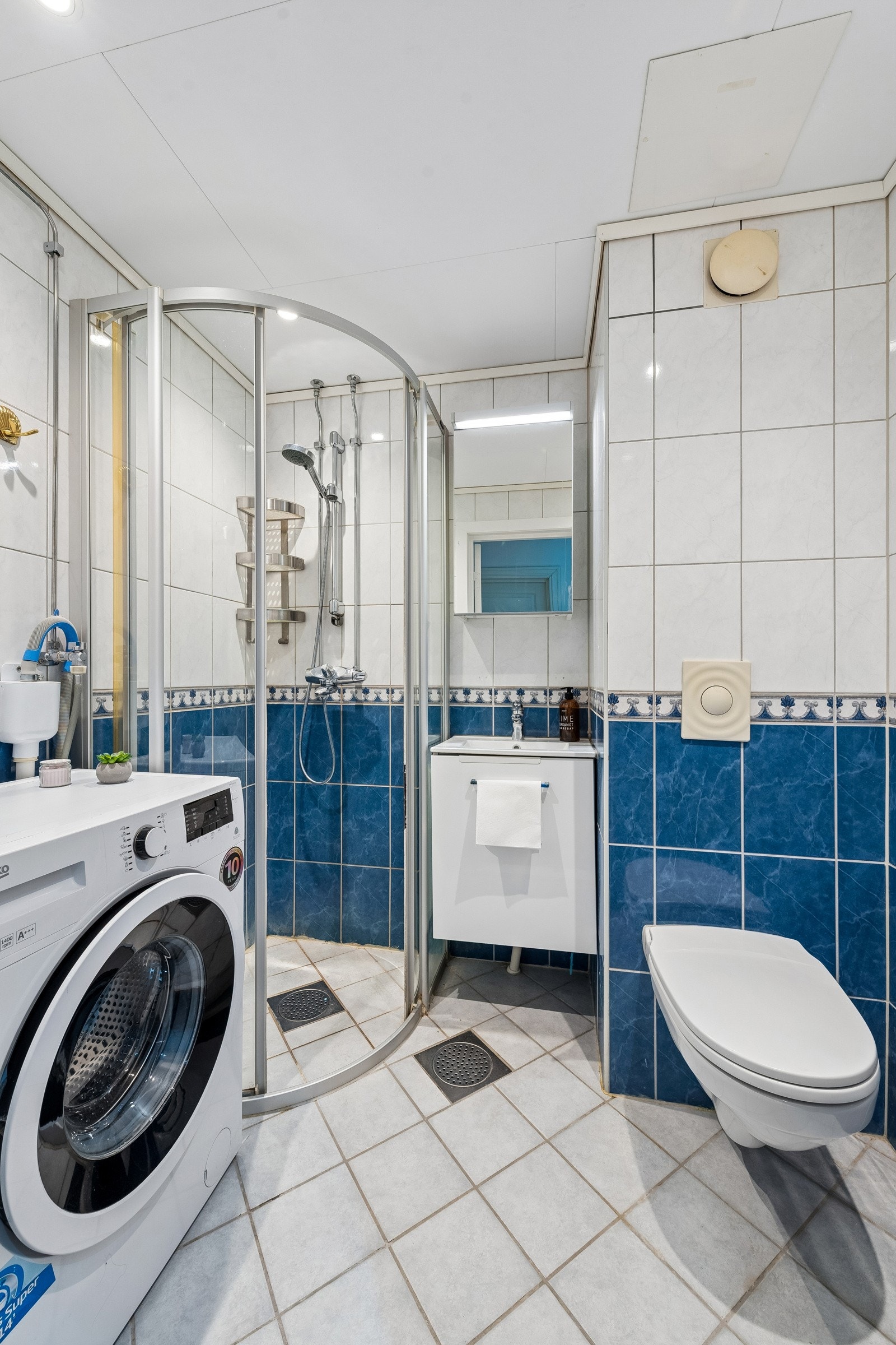 Badet er innredet med veggmontert klosett, dusjhjørne, servant med underskap, speil med overlys og opplegg for vaskemaskin. Ny himling og spotter i 2025. Galleribilde