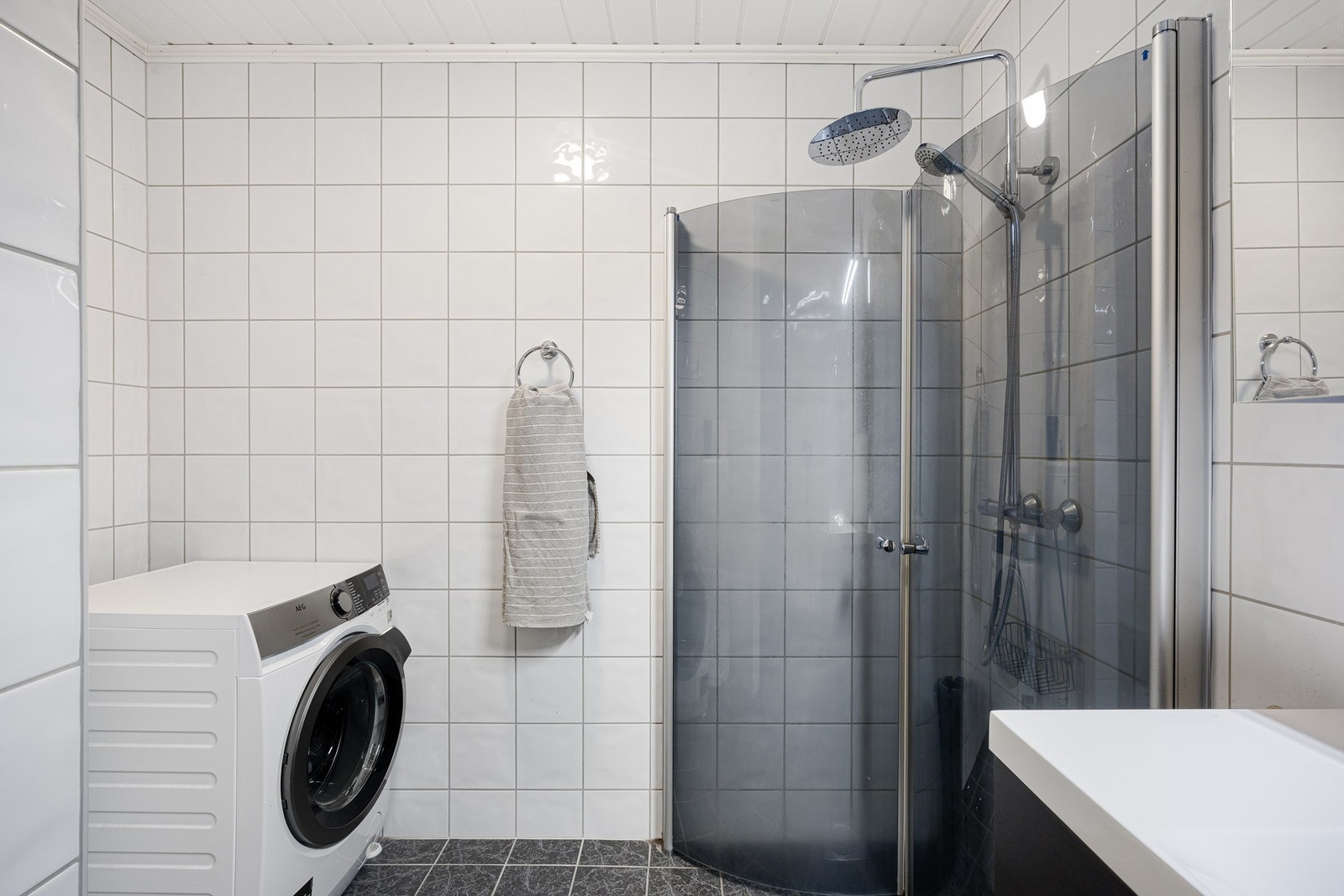 Badet er kombinert vaskerom med opplegg for vaskemaskin. Dusjhjørnet har svingdører og regnfallsdusj. Galleribilde