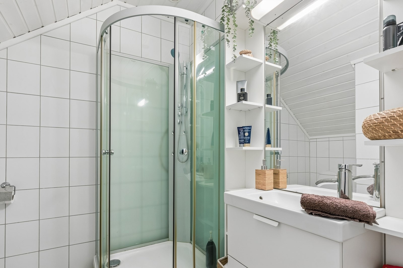 Badet i 2. etasje er helfliset og er innredet med gulvvarme, dusjkabinett og toalett. Den øvrige innredningen består av et speil med lys og et hvitt servantskap med tilhørende hyller. Galleribilde