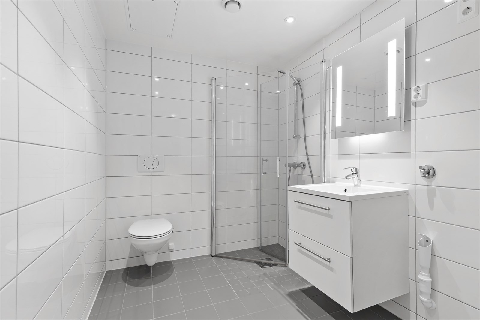 Badet er innredet med servant nedfelt i innredning, veggmontert toalett, dusjløsning med vegger/hjørne og opplegg for vaskemaskin. Galleribilde