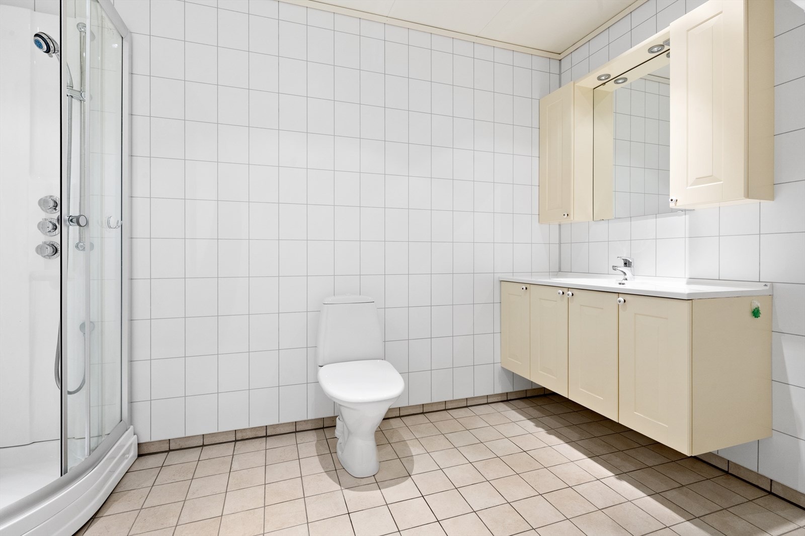 Lyst og nøytralt innredet bad med flislagt gulv og baderomsplater på vegger. Galleribilde