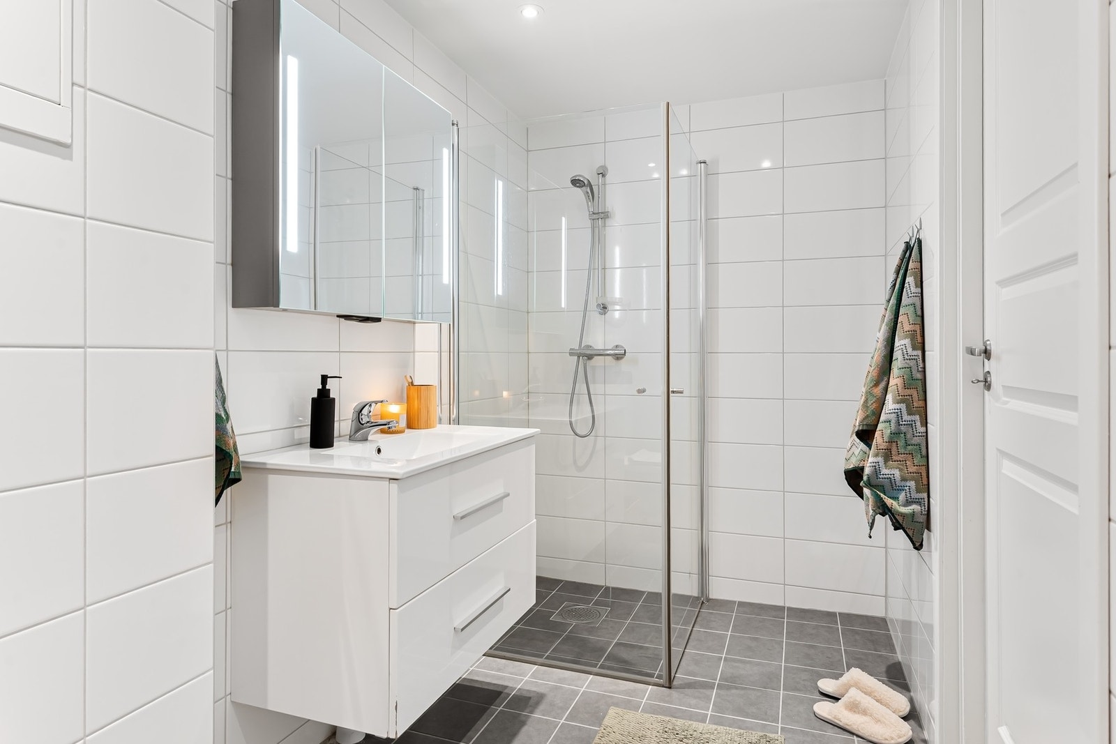 Badet er rehabilitert av borettslaget ca. 2019. Flislagt med varmekabler i gulv. Dusjnisje, hvit pen innredning med servant og speilskap, veggfestet WC og plass til vaskemaskin og tørketrommel Galleribilde