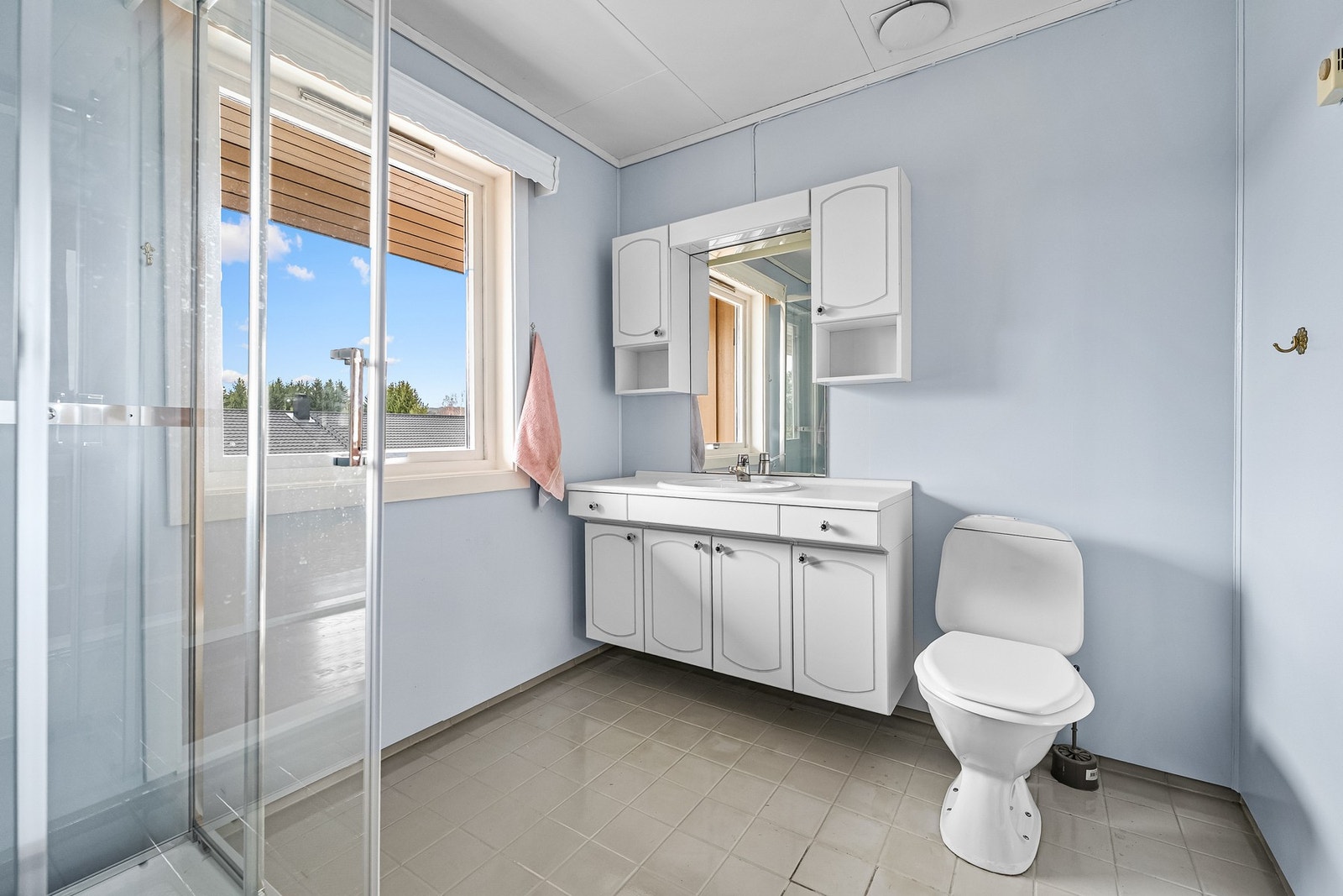 Badet i hovedetasjen er fra byggeår og har malte veggflater, samt flislagt gulv. Innredningen består av servantmøbel med over- og underskap, speil, toalett og frittstående dusjkabinett med glassdører. Galleribilde