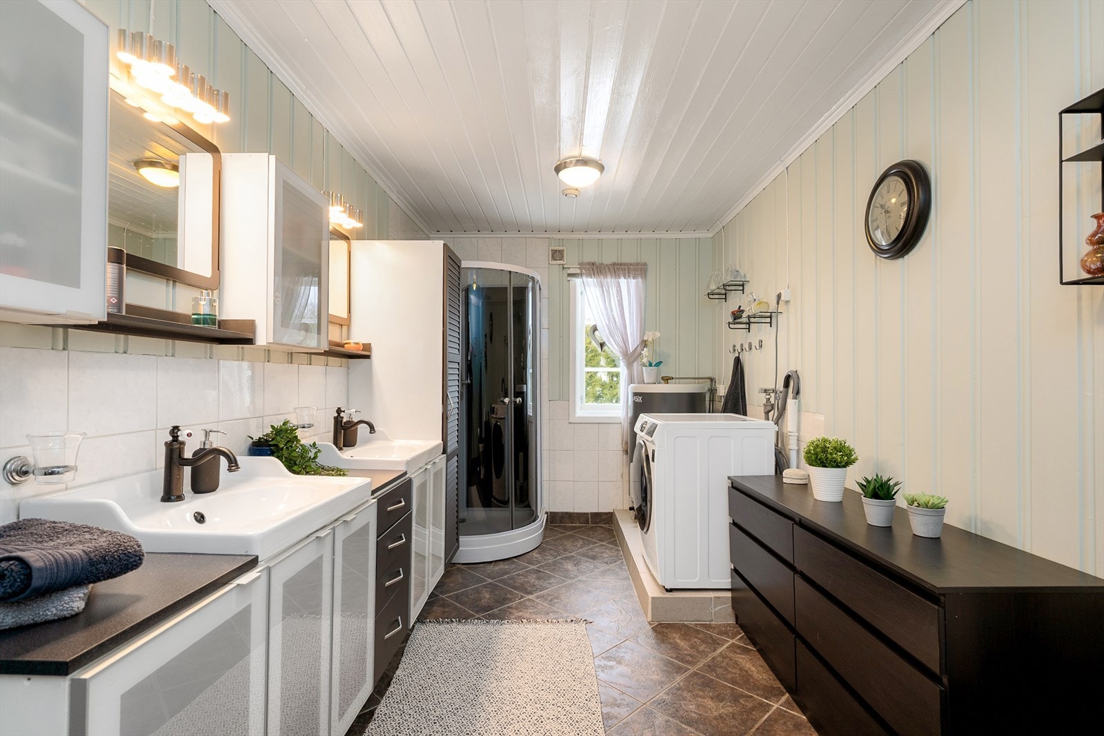 Badet har flislagt gulv med gulvvarme, dusjkabinett og opplegg for vaskemaskin. Galleribilde