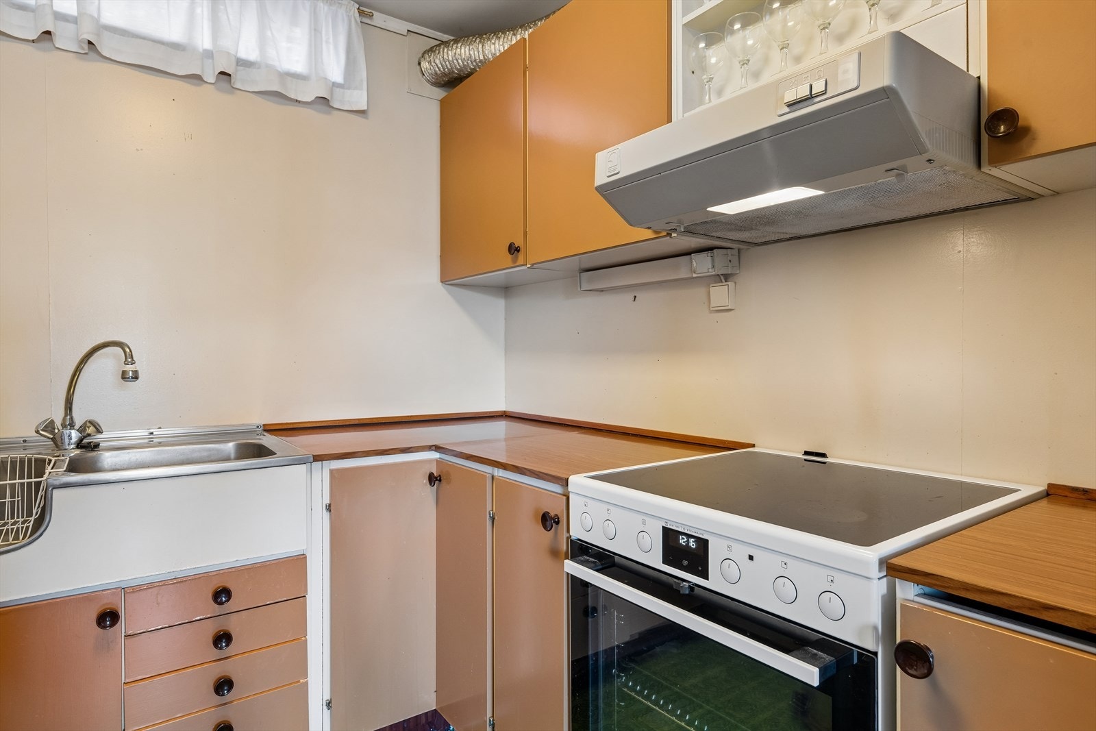 Kjøkkenet har innredning med glatte fronter, laminert benkeplate og vask i metall. Det er frittstående komfyr og ventilator med avtrekk ut. Galleribilde
