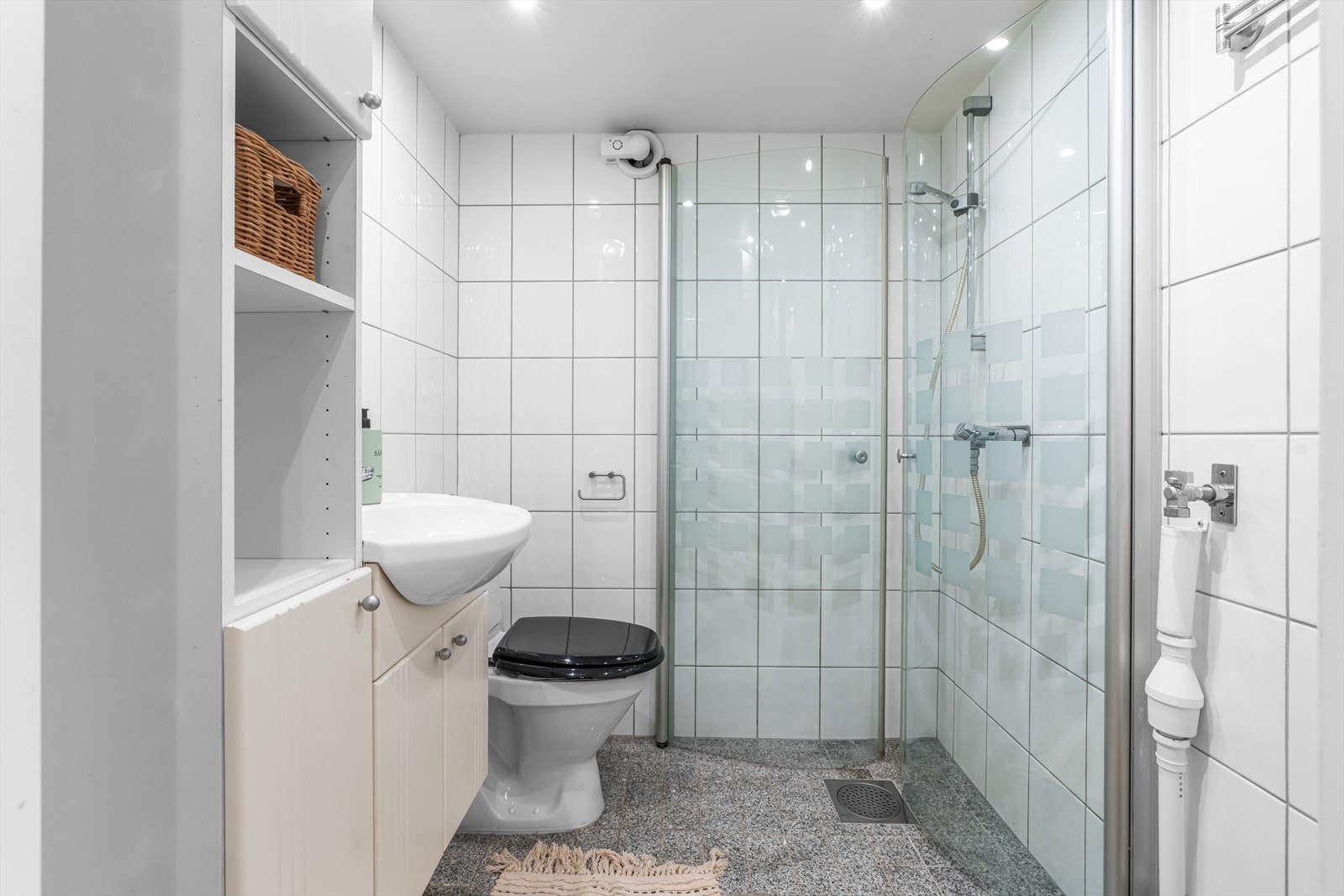 Eldre flislagt baderom med varmekabler i gulv og opplegg for vaskemaskin. Badet inneholder servant, toalett og dusj. Galleribilde