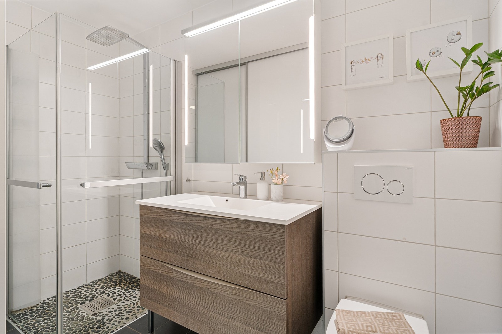 Badet er utstyrt med dusjgarnityr på vegg, pen innredning med servant og vegghengt toalett. Galleribilde