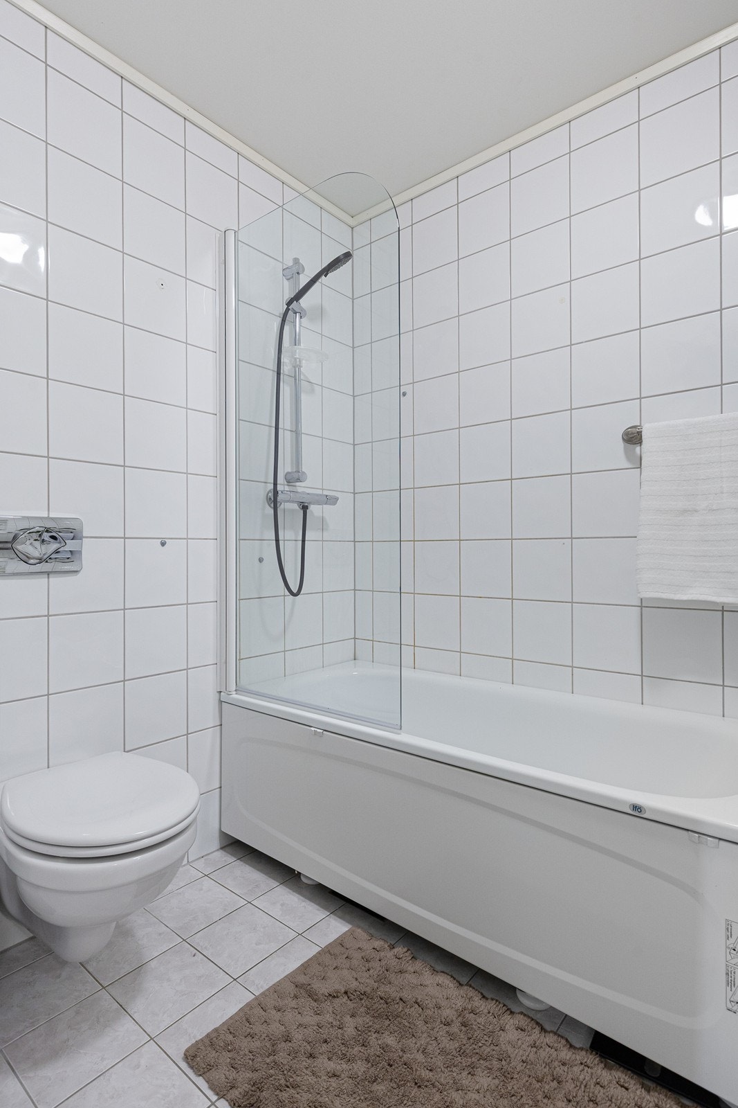 Bad er flislagt fra gulv til tak, med vegghengt wc, badekar med dusjmulighet, opplegg for vaskemaskin, og baderomsinnredning med heldekkende servant Galleribilde