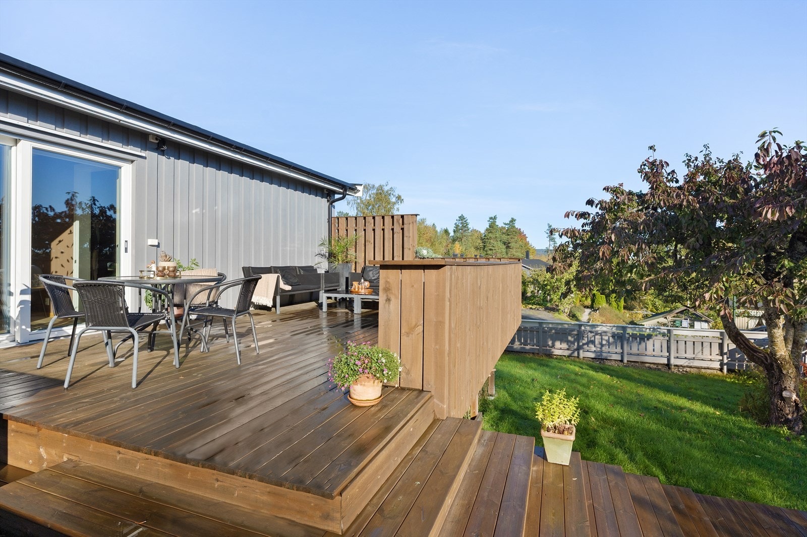 Solrik terrasse utenfor stuen med trapper ned til hage. Hagen er pent opparbeidet og har flere frukttrær. Galleribilde