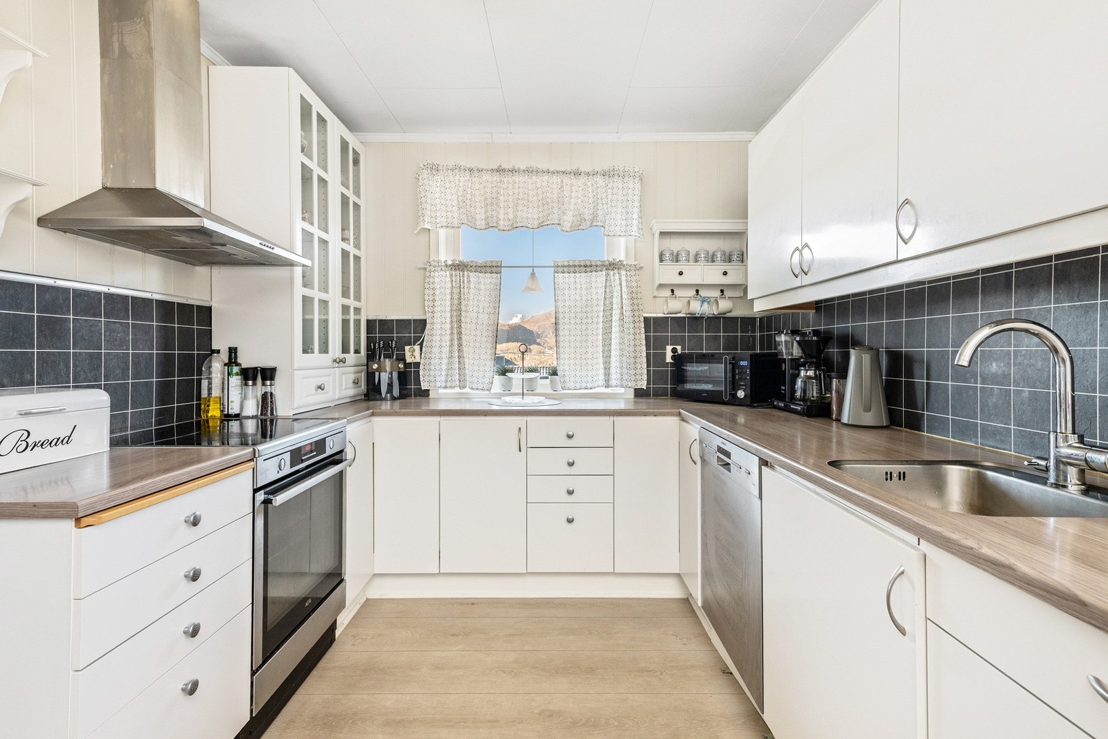 Kjøkkeninnredning med benker og skap med hvite, glatte fronter og laminat benkeplate. Galleribilde