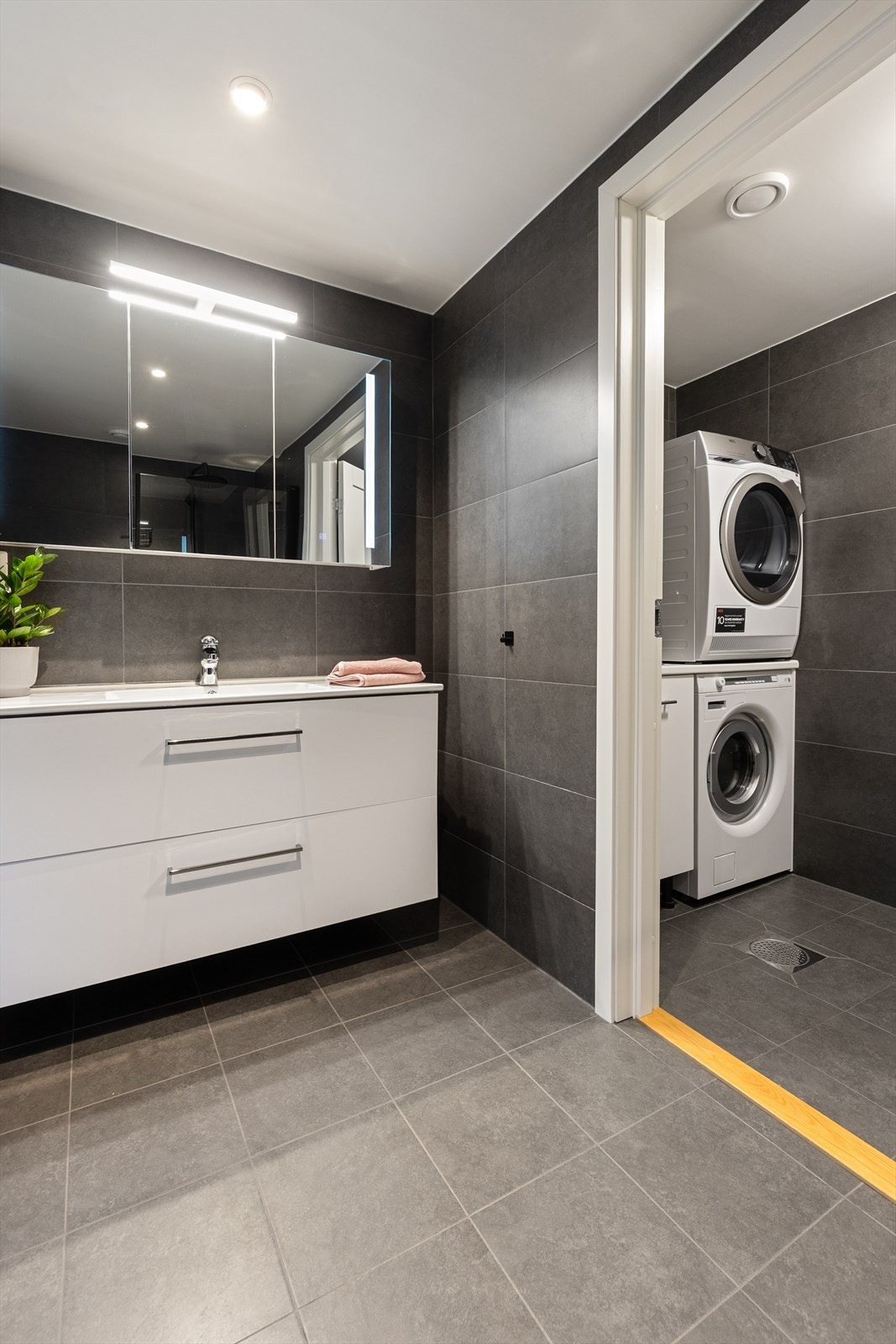 Innenfor badet er det et praktisk og avskjermet vaskerom med flis på gulv og vegger. Vaskerommet har innredning med underskap og nedfelt vask, samt opplegg for vaskemaskin og tørketrommel. Det er varmekabler i gulv og balansert ventilasjon. Galleribilde