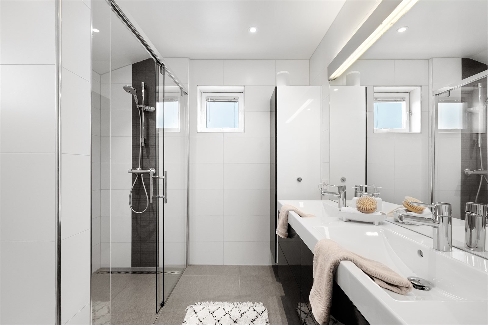Badet er moderne innredet med romslig dusjnisje med dobbel dusjløsning, vegghengt toalett, dobbel servant og bredt speil med belysning. Galleribilde