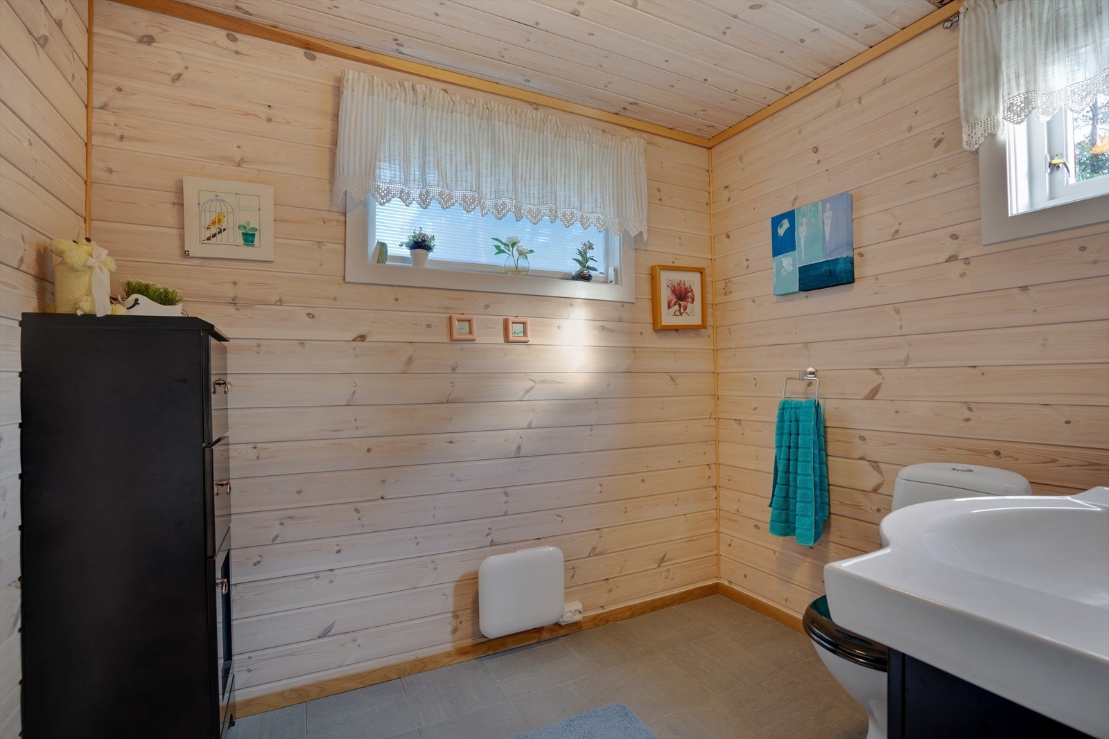 Baderom har flislagt gulv og panel på vegg og tak. Toalett og baderomseksjon med servant Galleribilde