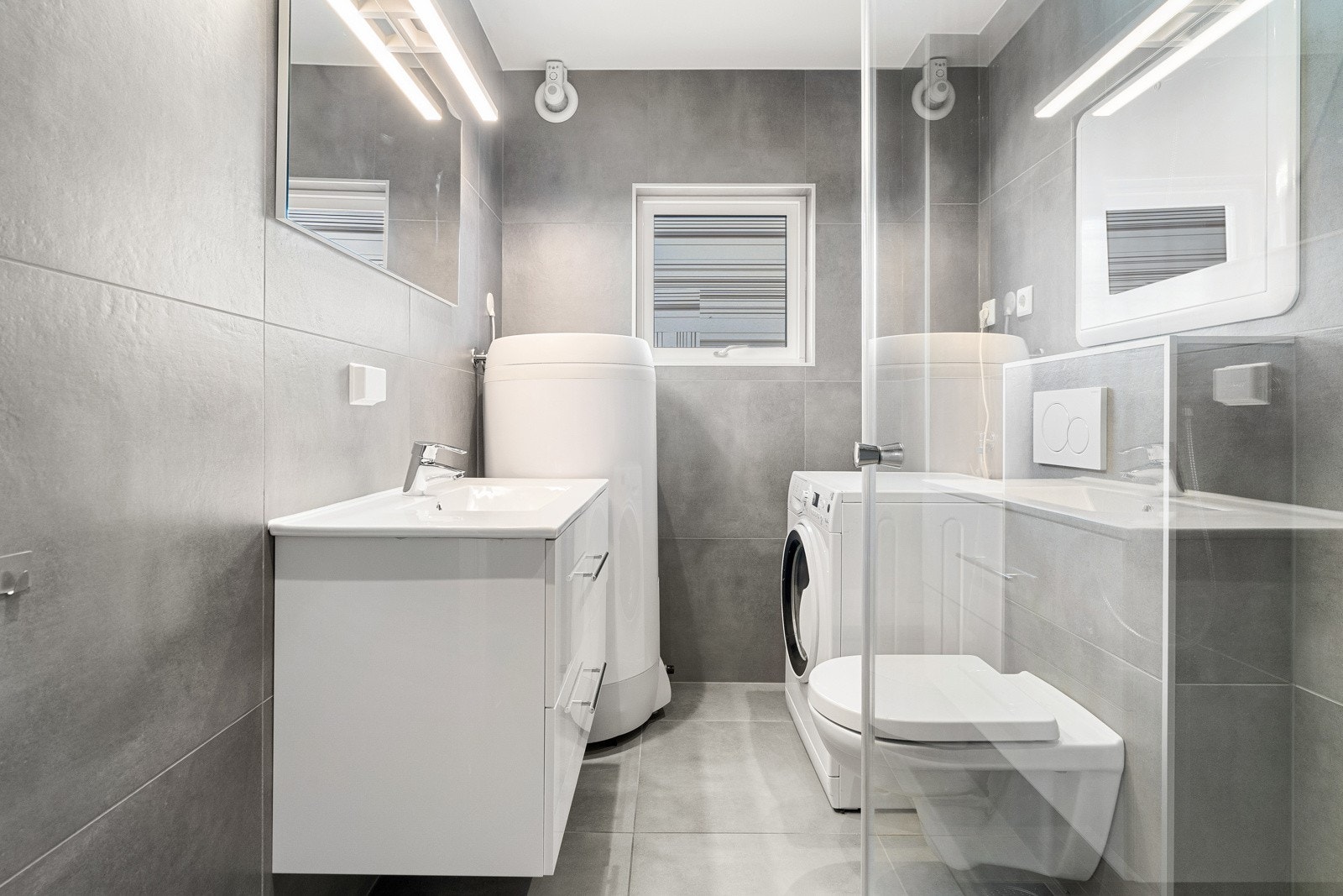 Moderne bad innredet med servant med oppbevaringsplass i skuffer, dusjhjørne, toalett og vaskemaskin.