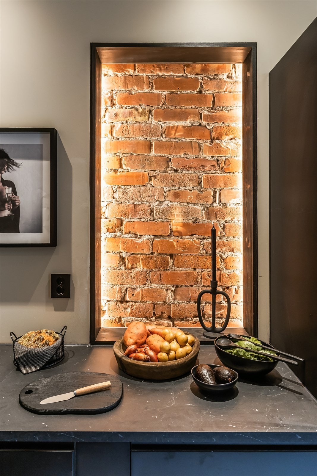 Tross moderne materialvalg er deler av den originale teglveggen rammet inn på kjøkkenet, som en flott detalj typisk for den klassiske bygården. Det er installert ledlys rundt teglsteinen og under benkeplate på øy. Galleribilde