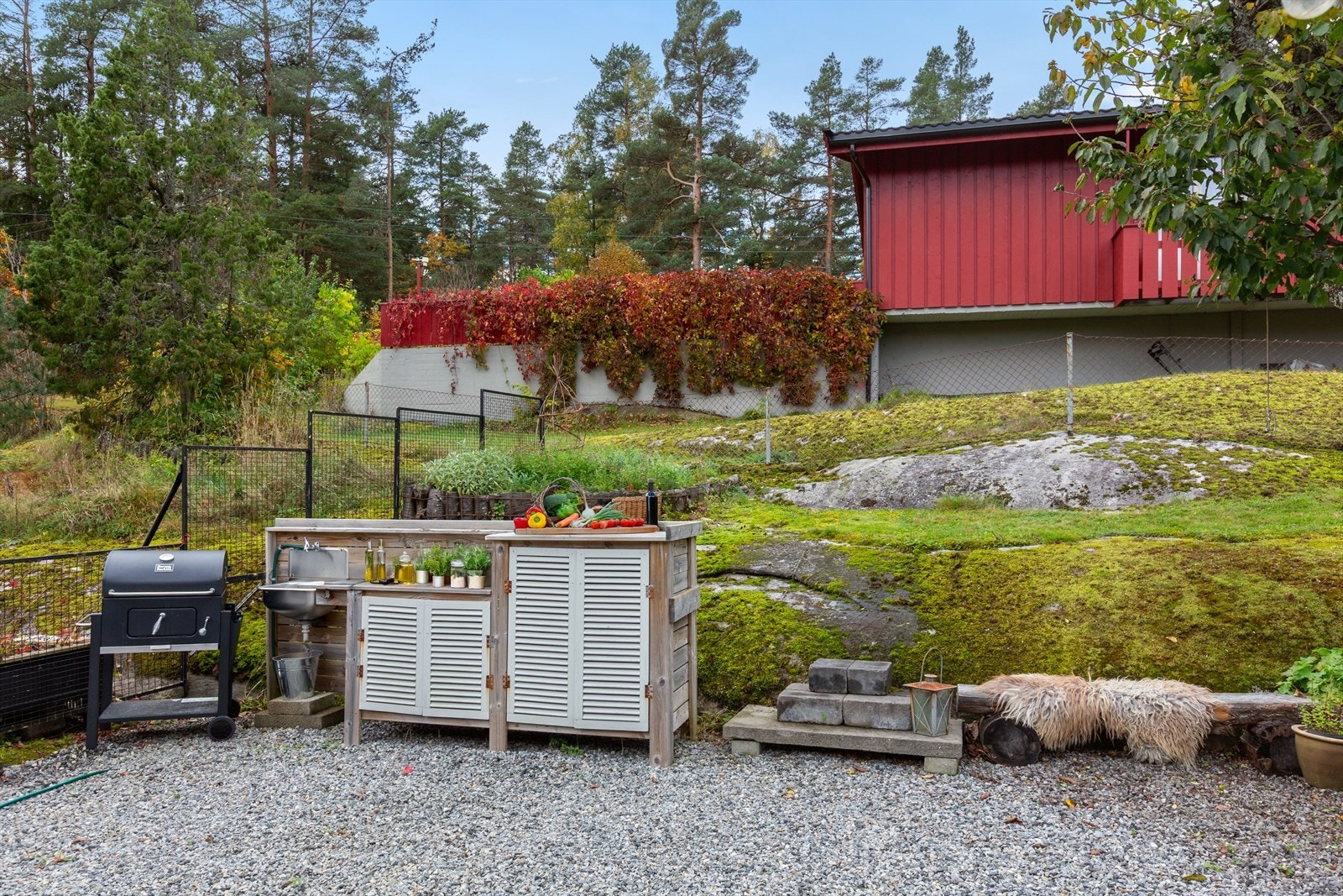 Stor gruset uteplass med utekjøkken og plass til spisebord og sittegruppe. Galleribilde