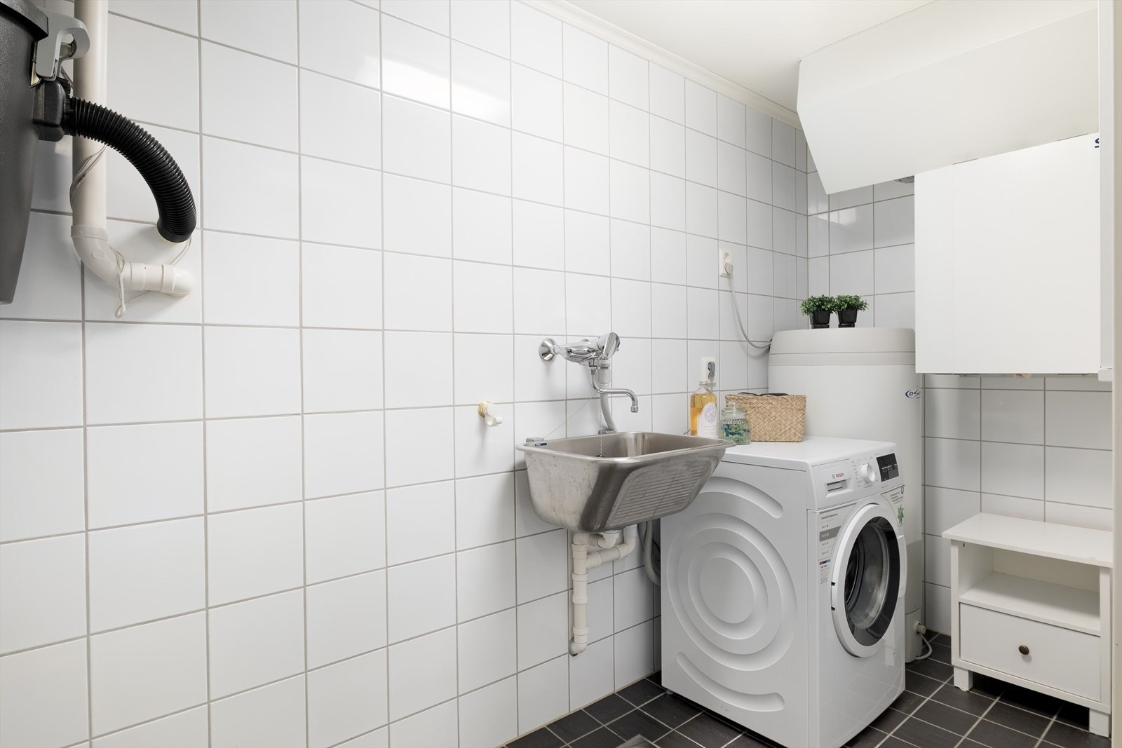 Heilflisa vaskerom med varmekablar i golv. Rommet er funksjonelt innreia med utslagsvask og opplegg for vaskemaskin. Elles er varmtvannstank, sentralstøvsugar og sikringsskåp plassert i dette rommet. Galleribilde