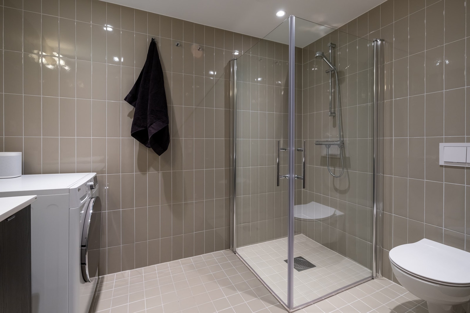 Videre er det vegghengt toalett og dusjhjørne med innfellbare glassdører. Baderommet har også opplegg for vaskemaskin og plass til tørketormmel. Galleribilde