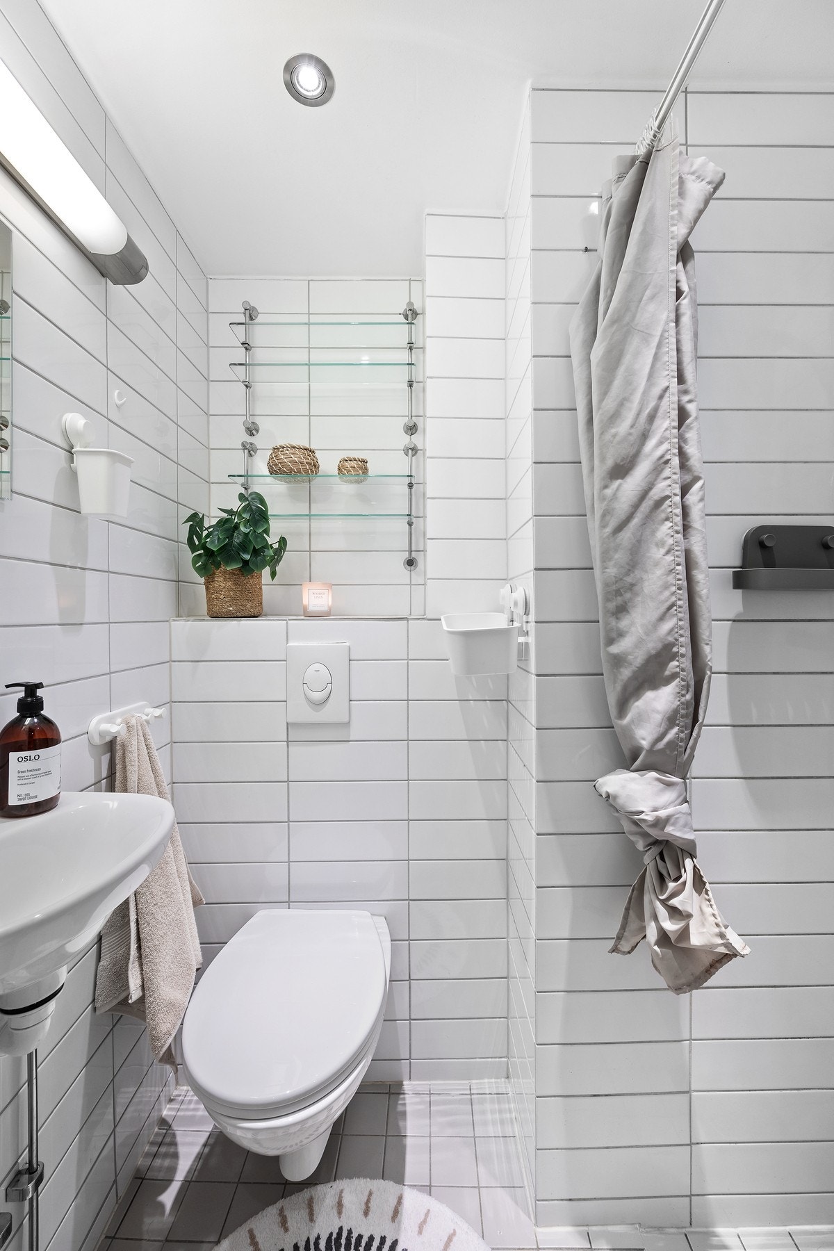 Flislagt baderom med vegghengt wc, servant, veggspeil med belysning og downlights i taket. Galleribilde