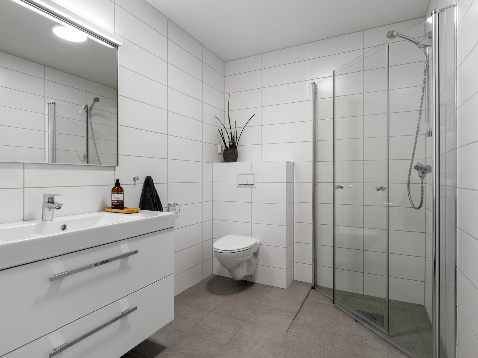 Badet i andre etasje har gulvfliser med gulvarme og hvite veggfliser. Baderomsinnredningen består av en heldekkende servant på en mørk skuffeseksjon og speil med belysning. Galleribilde