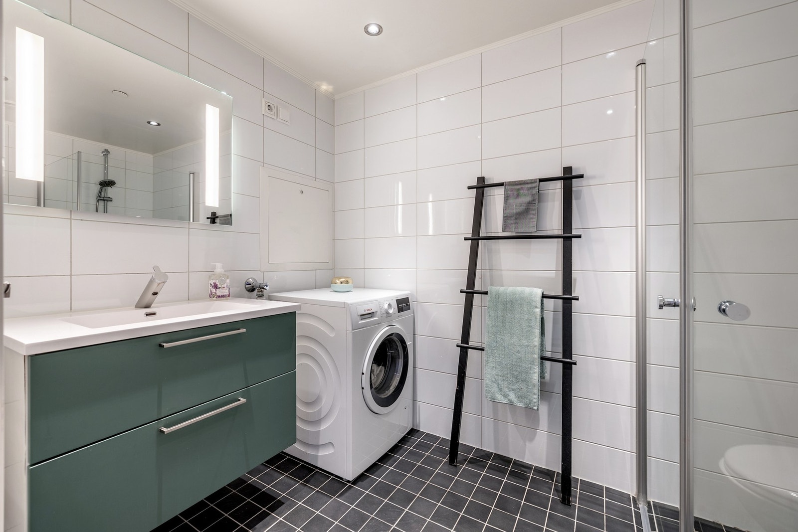 Badet har et stilrent uttrykk med flislagte vegger- og gulv, varmekabler, innfelt downlights og opplegg for vaskemaskin. Galleribilde