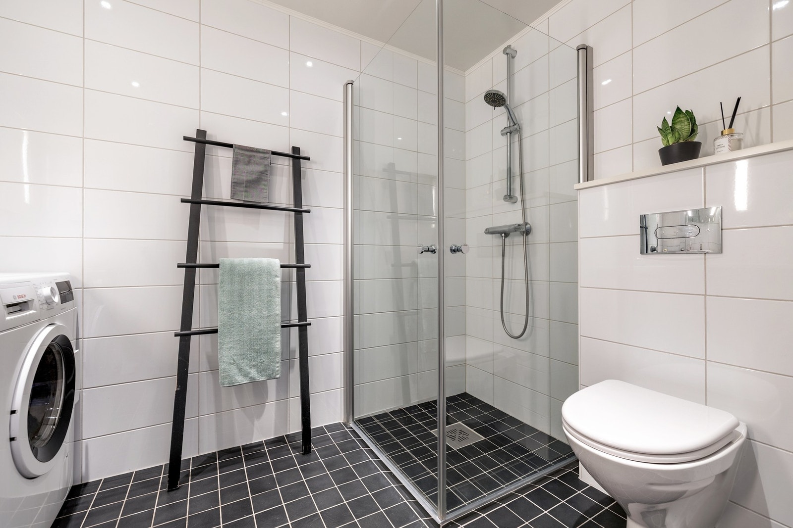 Badet er innredet med servantinnredning, speil på vegg over servant, vegghengt toalett og dusjhjørne med svingbare glassdører. Galleribilde