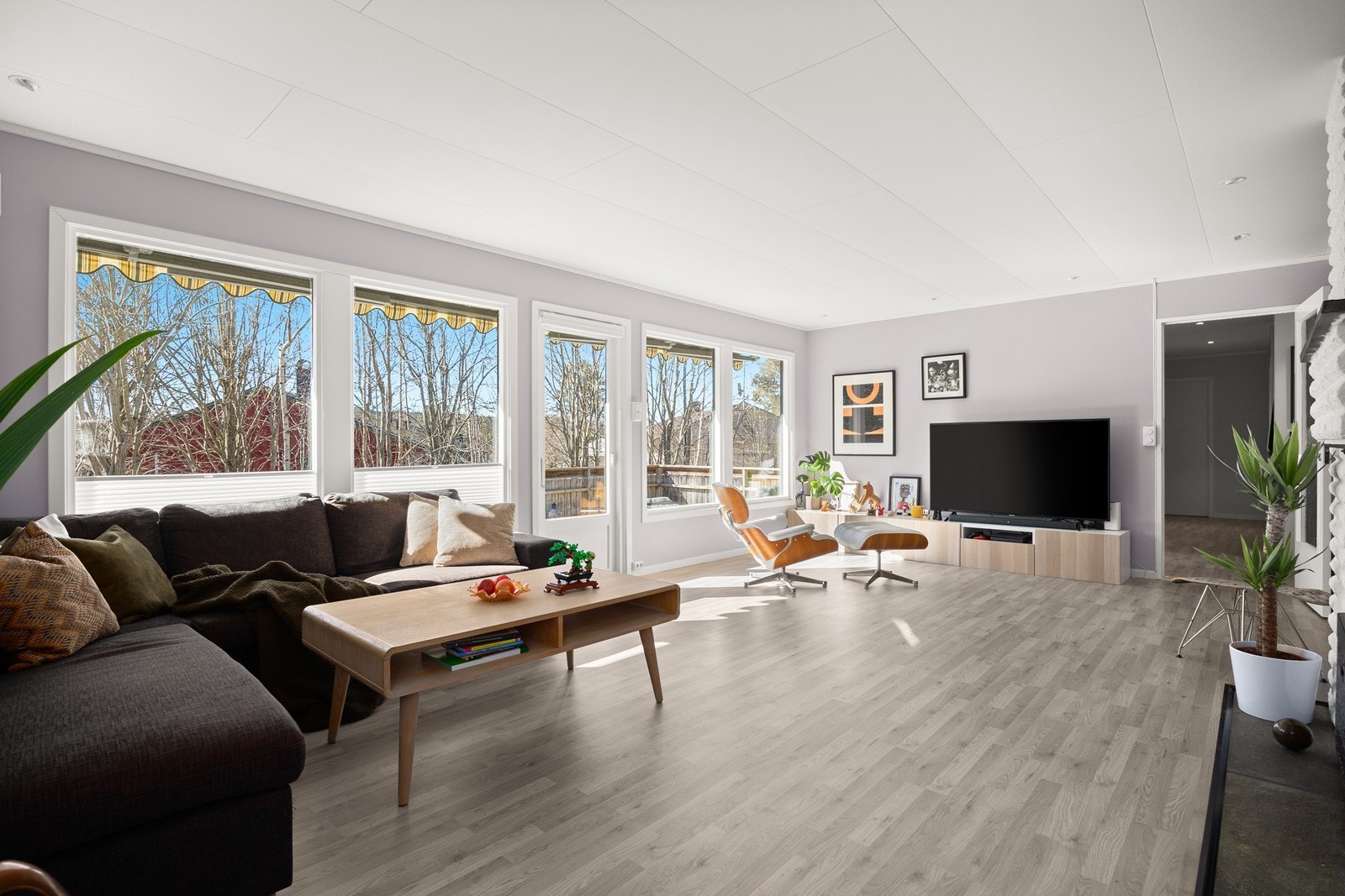 Romslig stue og spisestue med laminat på gulv og malte plater på vegger. Åpen peis. LED downlights i tak Galleribilde