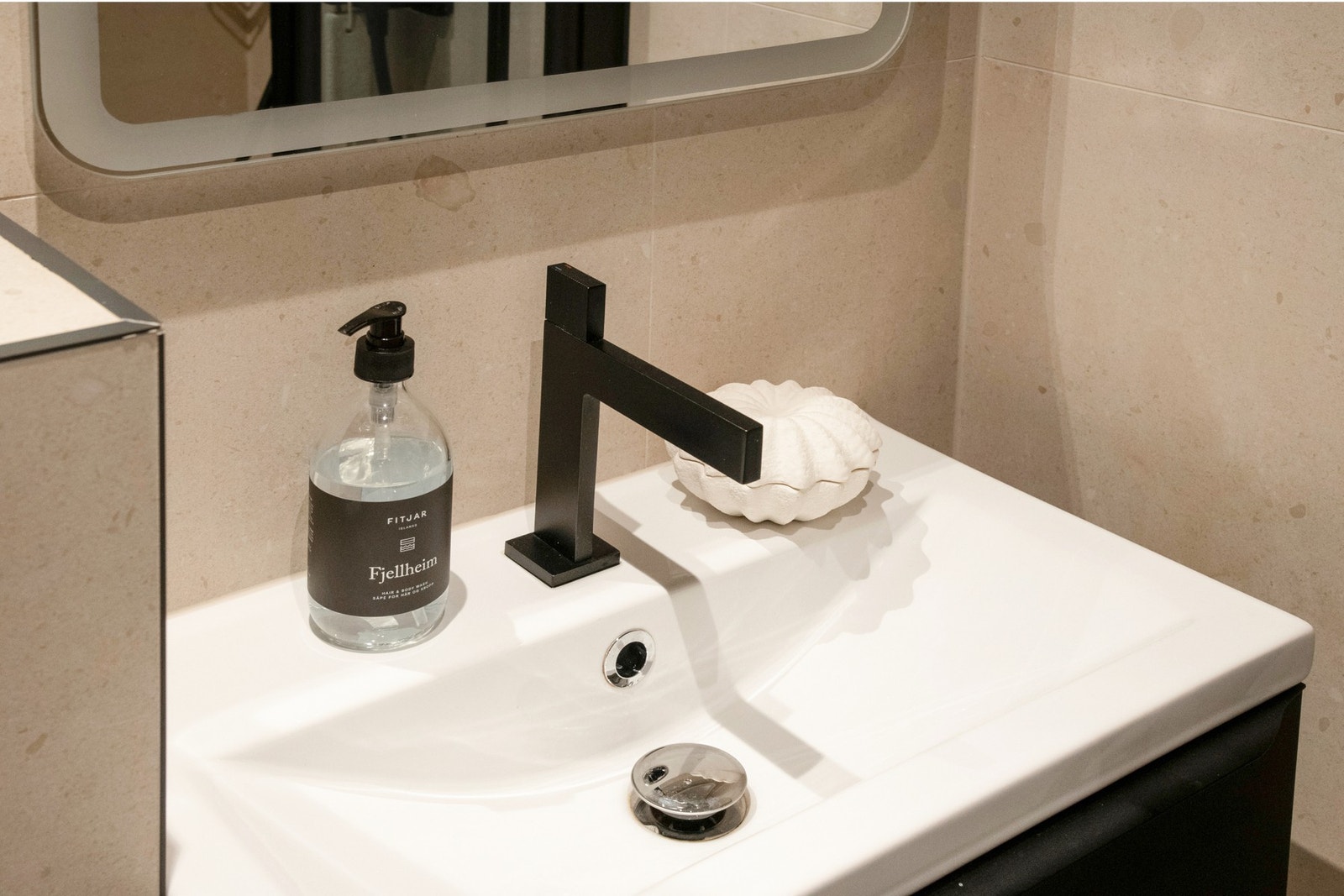 Badet har flislagte overflater og varmekabler i gulv. Badet er utstyrt med servantinnredning, toalett og dusjhjørne med både regn- og hånddusj. Galleribilde