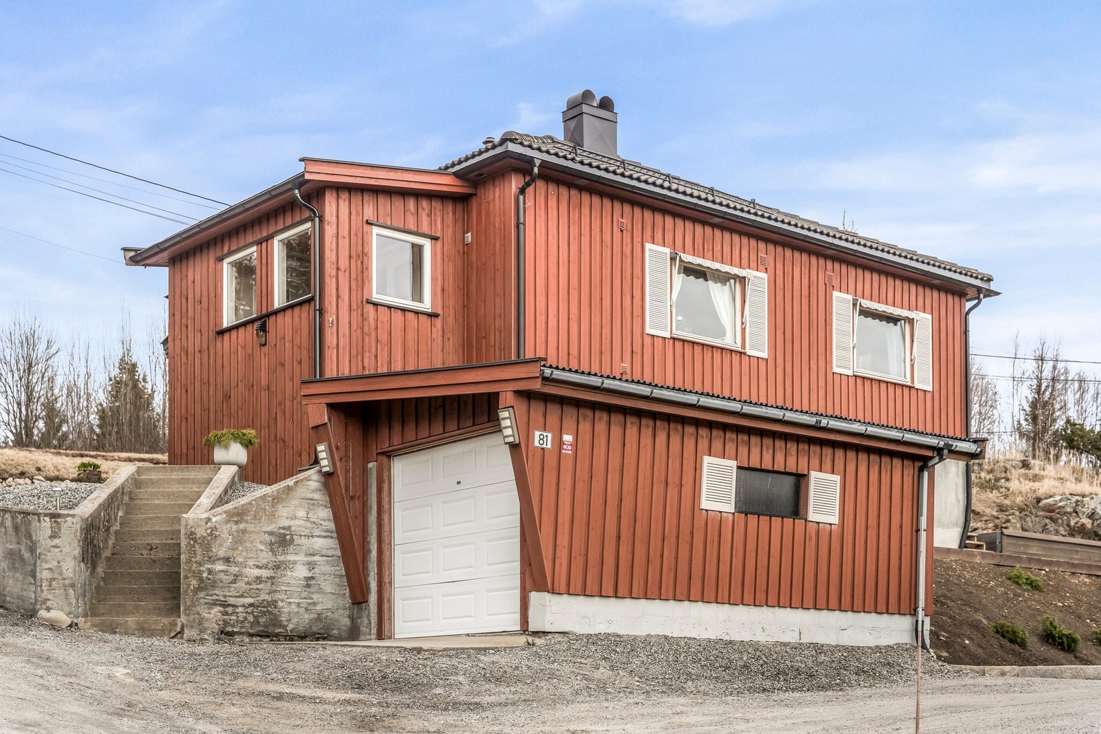 Rødmalt hus med hvite vinduskarmer og garasje i underetasjen. Trapp opp til inngangsparti. Galleribilde
