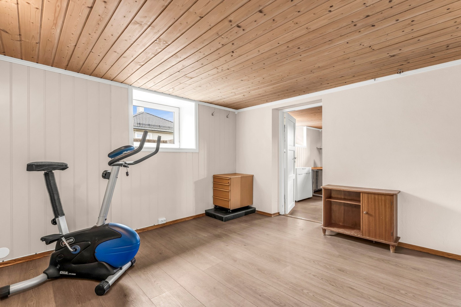 Rommet har panelvegger, tregulv og et vindu som gir naturlig lys. Det er tilknyttet et tilstøtende rom. Galleribilde