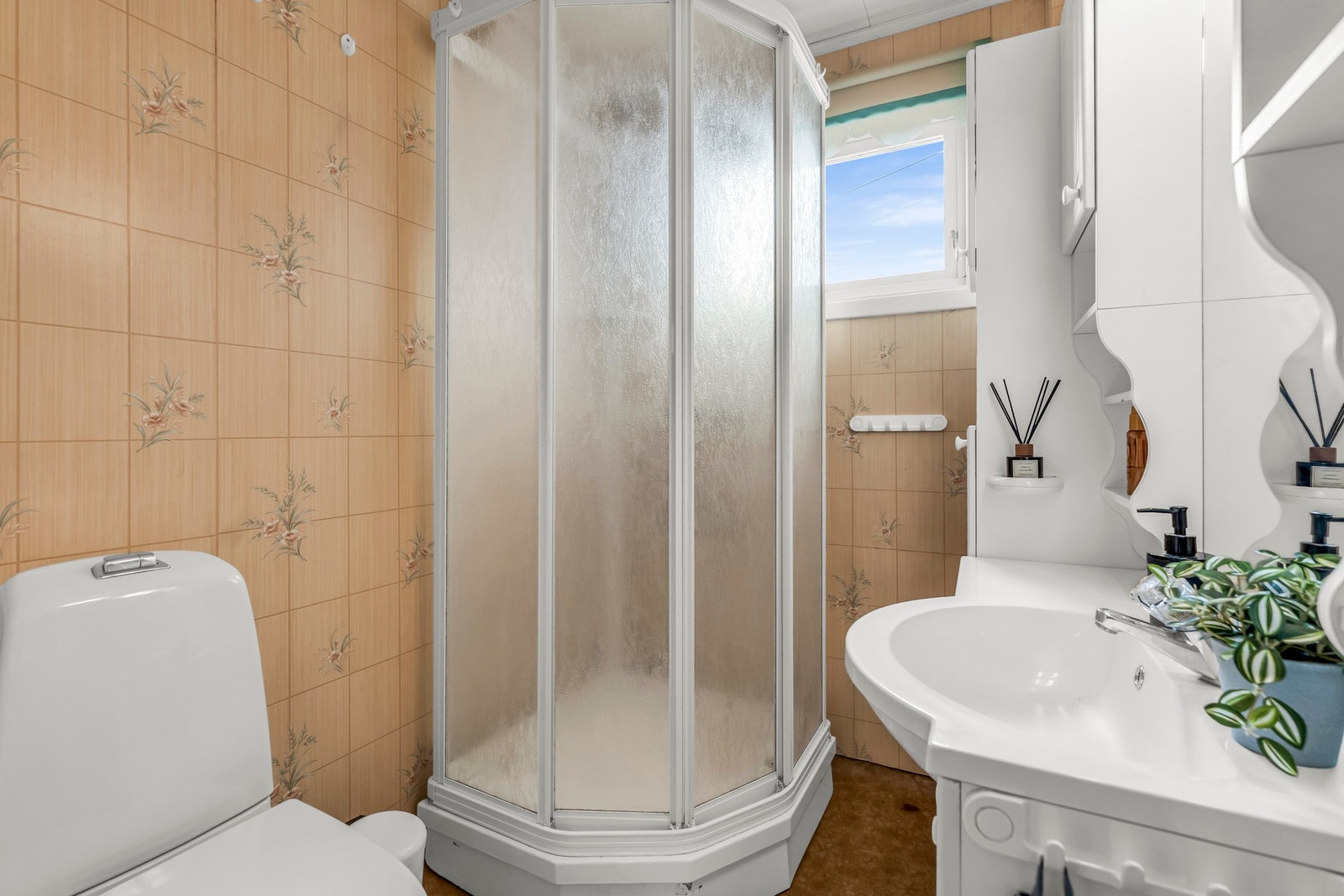 Badet har dusjkabinett, toalett og servant med speilskap. Veggene er flislagt og det er et vindu for naturlig lys. Galleribilde