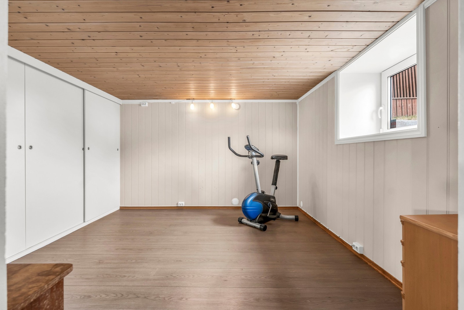 Lyst rom med panelvegger, tregulv og vindu som slipper inn naturlig lys. Galleribilde