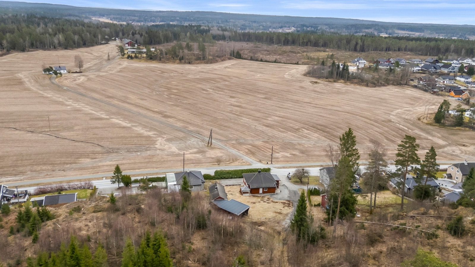 Boligen ligger i et landlig område med store åkrer og skogkledde åser i bakgrunnen. Galleribilde