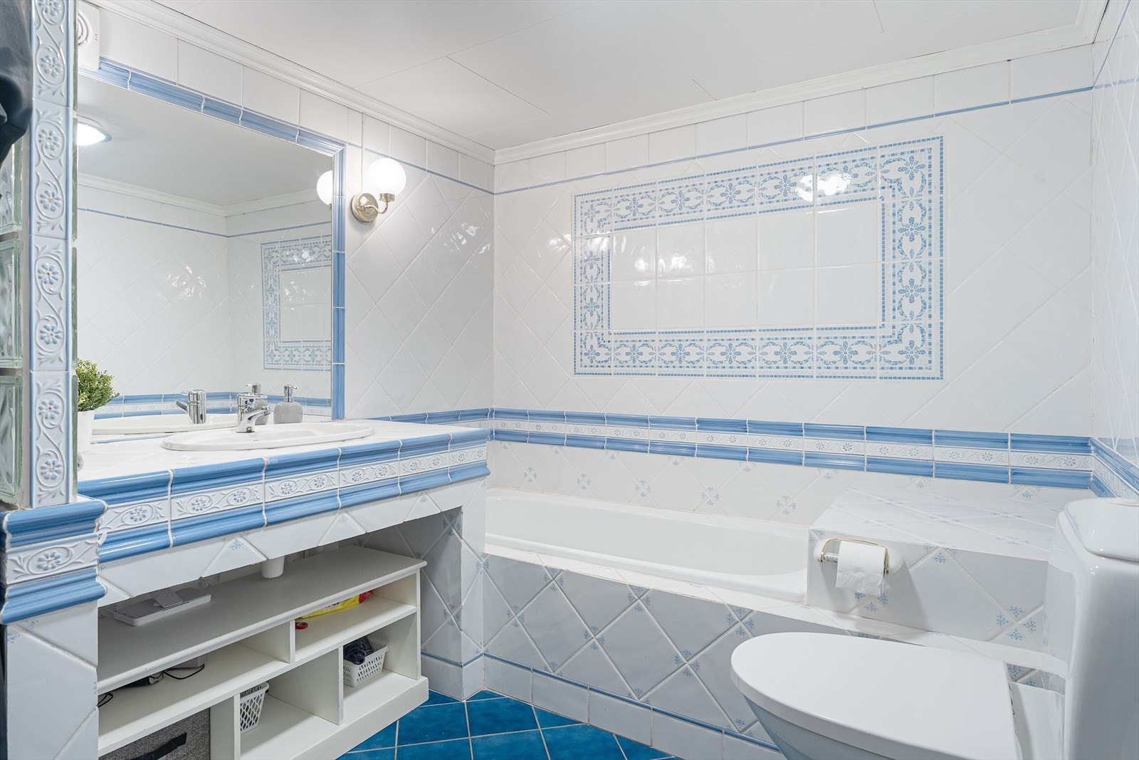 Badet har fliser på gulv og vegger samt prefabrikkerte plater i himling - badet er innredet med plassbygd flislagt innredning med nedfelt servant, vegghengt toalett, flislagt innebygget badekar og stor dusjnisje med glassbyggerstein Galleribilde