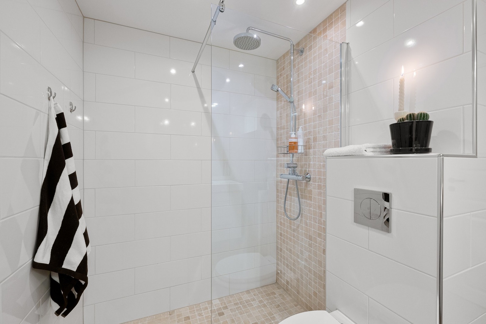 Badet er utstyrt med en romslig dusjnisje med glassvegg og termostatstyrt dusjbatteri i krom med både kran- og hånddusj, vegghengt toalett med innebygget sisterne og veggmontert servantinnredning med heldekkende vask og ett-greps armatur i krom. Galleribilde