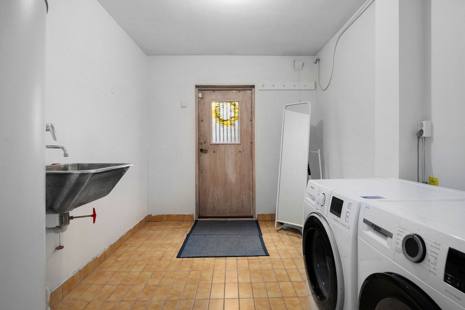 Funksjonelt vaskerom med varmekabler, opplegg for vaskemaskin, utslagsvask og varmtvannstank, med direkte adkomst fra utsiden. Galleribilde