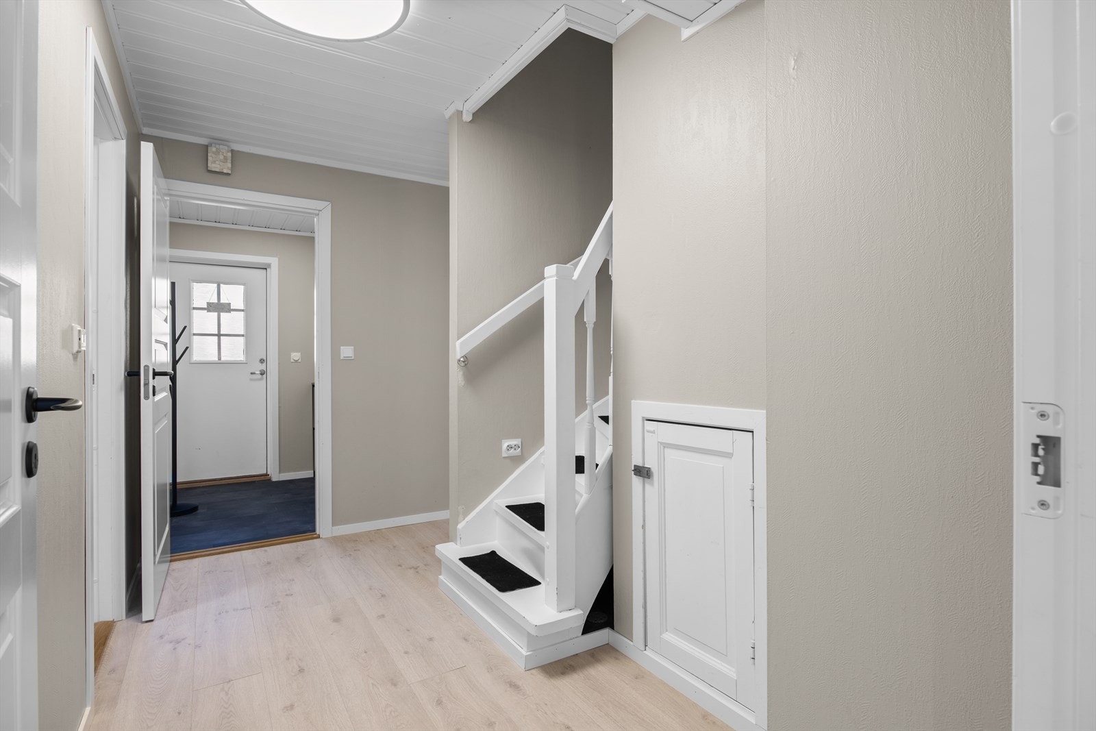 Fra gangen leder en tretrapp opp til andre etasje. Overflatene er gjennomgående med laminat på gulv og malte vegger. Galleribilde