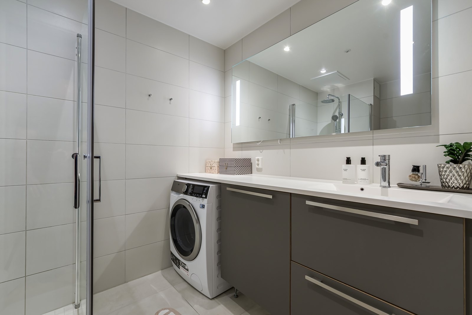 Badet består av dusjsone med glassdører, servant, veggheng toalett og opplegg for vaskemaskin. Galleribilde