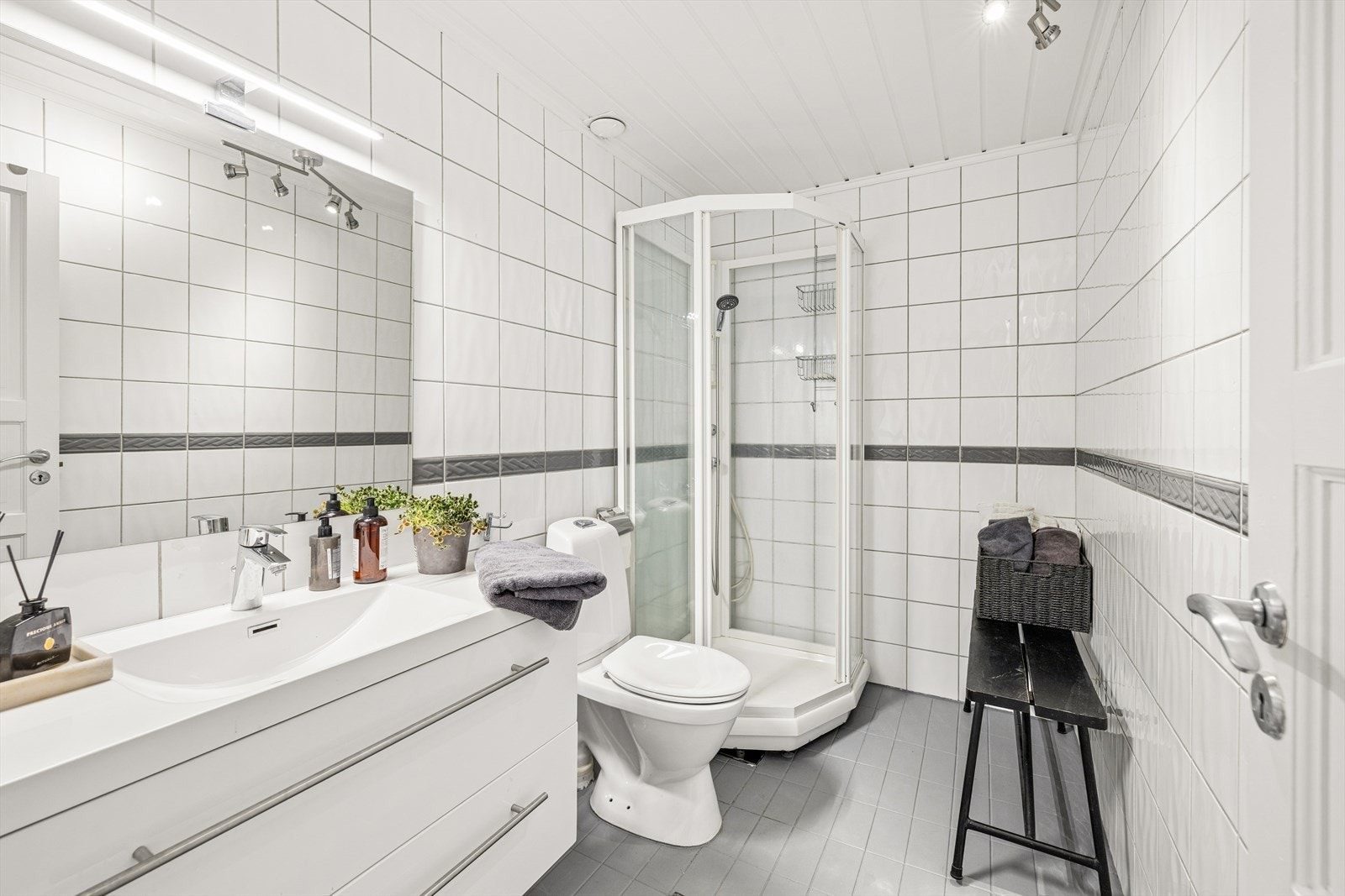 Bad i 2. etasje med fliser på vegger og gulv med gulvvarme. Badet har innreding med servant med underskap, speil med tilhørende belysning, dusjkabinett og gulvmontert wc. Galleribilde