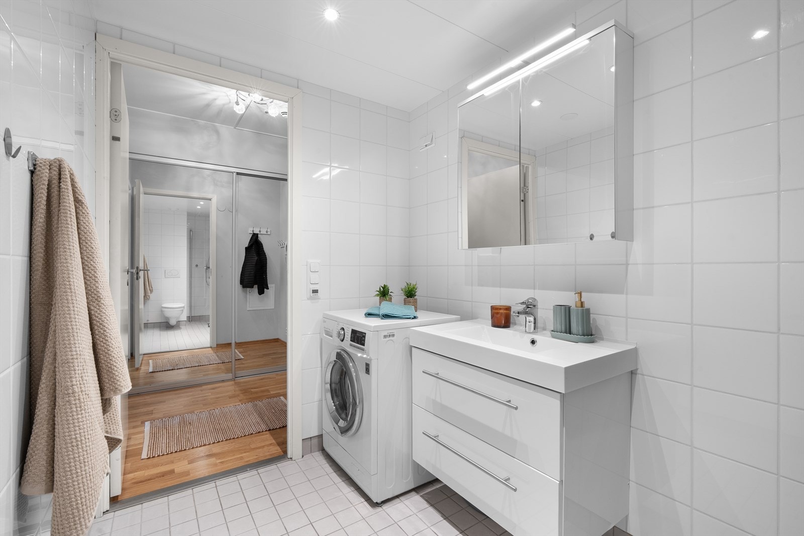 Badet er innredet med vegghengt toalett, servant nedfelt i innredning og speilskap med lys. Dusjhjørne med svingbare glassdører gir en praktisk løsning, og det er opplegg for vaskemaskin, samt mekanisk avtrekk. Galleribilde