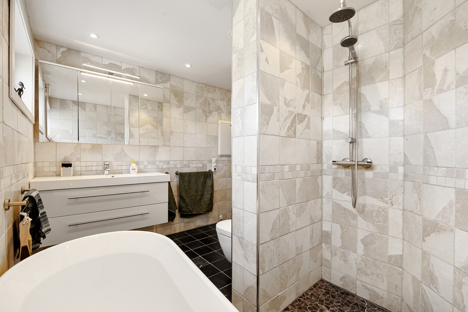 Badet har en god utforming med romslig dusjsone, badekar, toalett og moderne baderomsinnredning. Galleribilde
