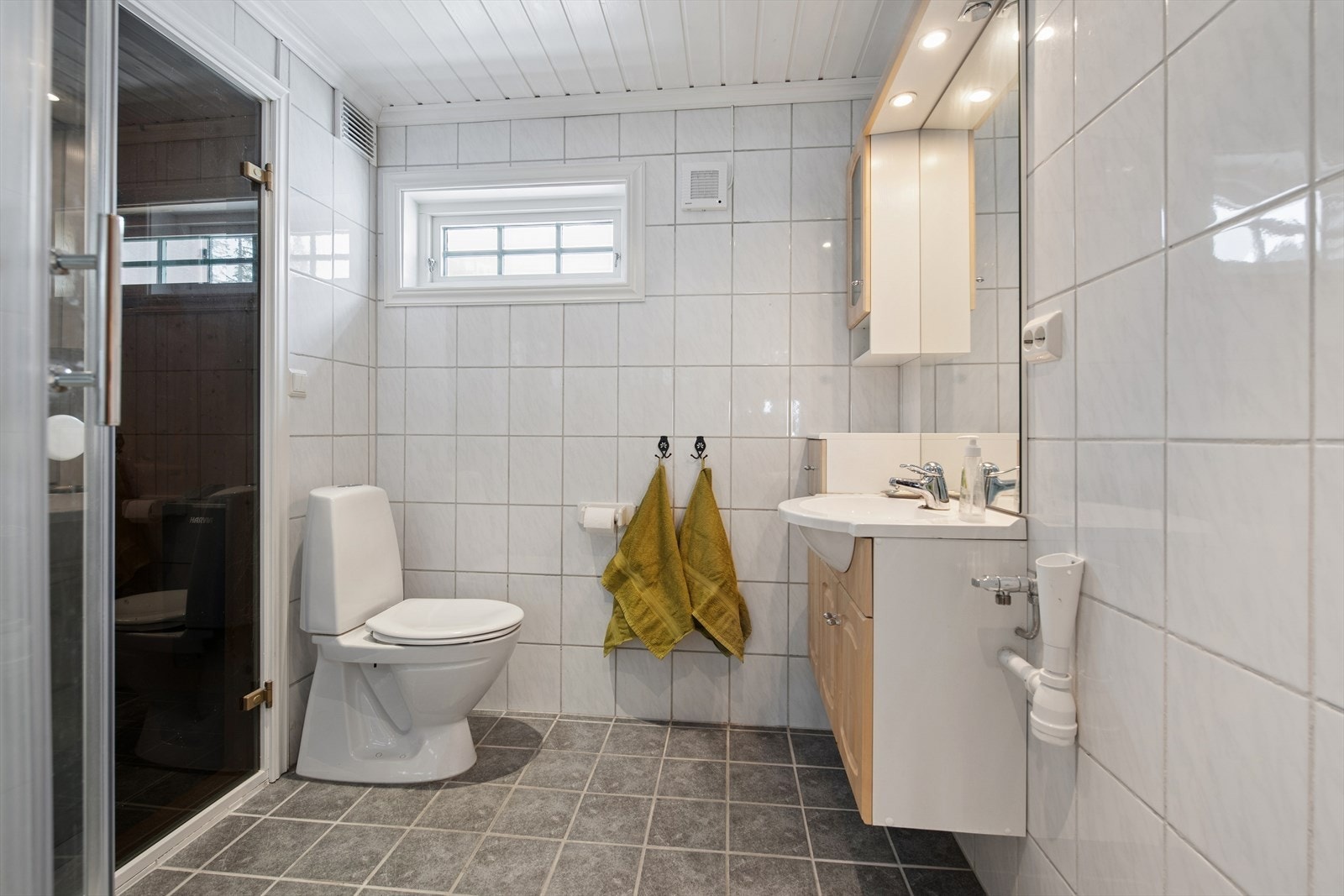 Badet har flislagte vegger og gulv, med elektriske varmekabler som gir en behagelig temperatur. Badet er innredet med servantskap med heldekkende servant og overskap, dusjkabinett, gulvstående toalett og opplegg for vaskemaskin Galleribilde