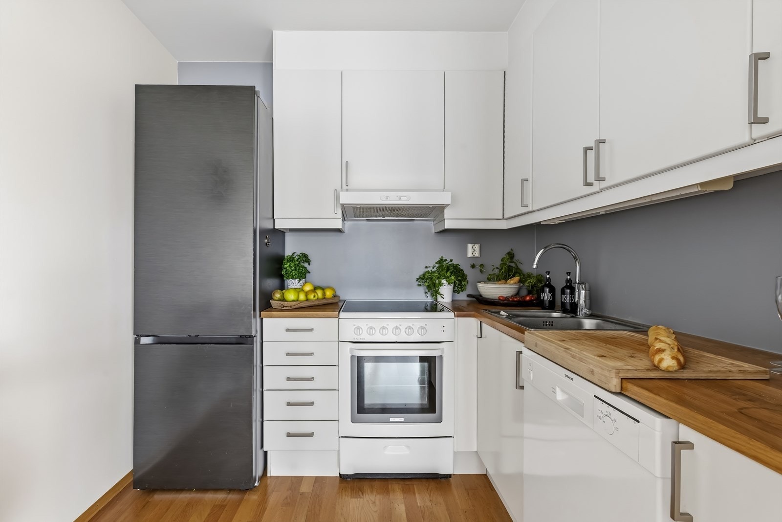 Kjøkkeninnredning med glatte folierte fronter, benkeplate i tre med nedfelt kum i rustfritt stål og ventilator tilsluttet kanal/ventilasjonssystem. Galleribilde