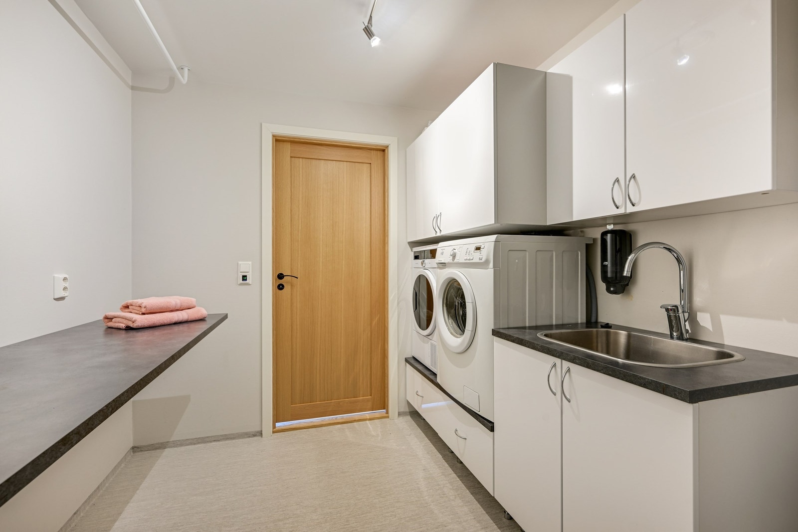 Praktisk vaskerom med opplegg til vaskemaskin og tørketrommel i tilpasset vaskeromsinnredning, samt innredning med nedfelt utslagsvask av stål. Galleribilde