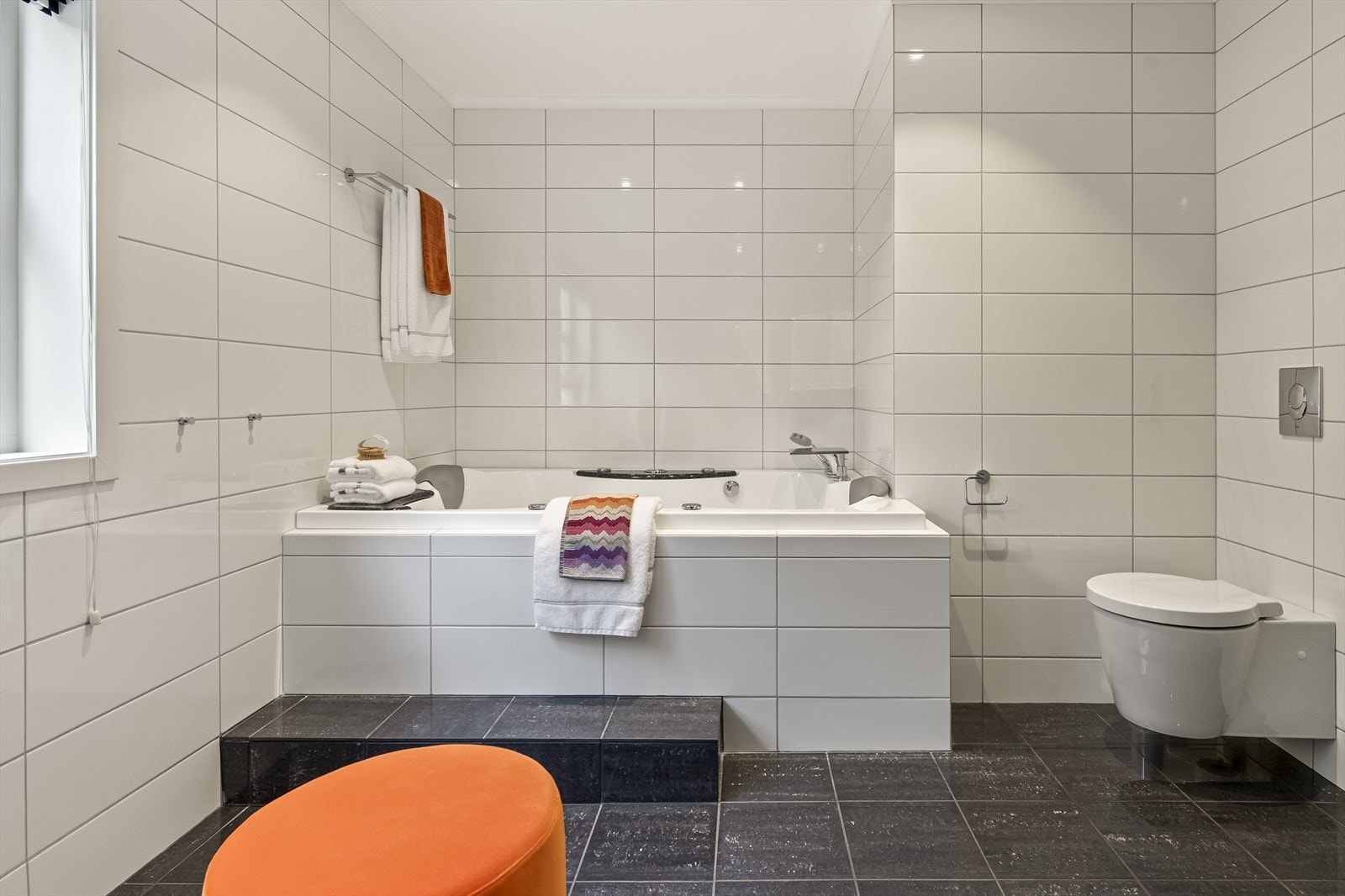 På badet er det både et innfliset boblebadekar og en dusjnisje med svingbar glassdør. Hvite veggfliser kombineres med mørkgrå gulvfliser i glasert effekt. Galleribilde